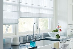 Sheer white roman shades adjusted to different heights in kitchen over sink