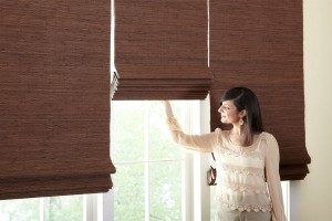 Woman standing looking out windows dark brown three cordless woven wood shades at various heights