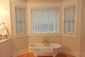 White wood blinds over bay window above antique bathtub
